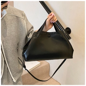 Detail of a black trapezoid tote bag with dual handles and long shoulder strap