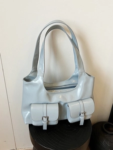 Light blue patent leather shoulder bag with front flap pockets on wooden base display
