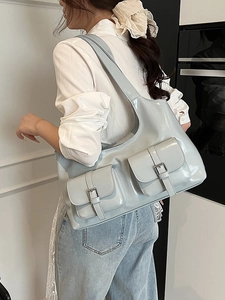 Light blue patent leather tote bag with front pockets shown on a shoulder