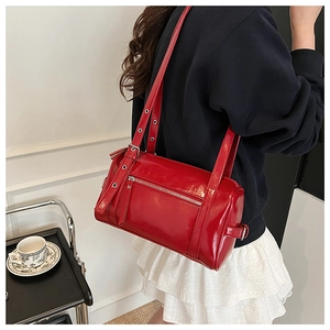 Close-up of red patent leather shoulder bag with metallic eyelet straps and silver zipper