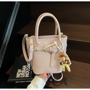 Close-up of pink lychee leather bucket bag with metal buckle and cute doll pendant