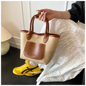 Close-up of woven straw tote bag with brown leather pocket and embossed detail