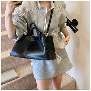 Minimalist black leather tote bag with top handles and adjustable shoulder strap worn by model