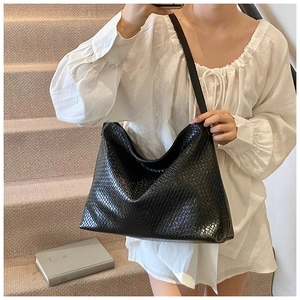 Detail of a large black woven leather hobo bag worn over the shoulder by a model