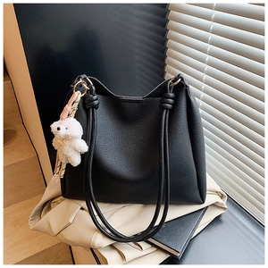Détail d'un sac seau noir en cuir litchi avec poignées corde et breloque ours