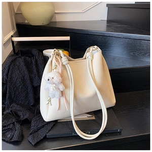 Détail du sac seau blanc crème à grain de litchi avec pendentif ours sur l'escalier