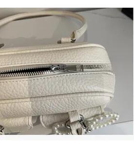 Detailed macro view of smooth silver zipper and pearl chain on cream pebble leather bag