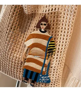 Makroansicht der beigefarbenen Häkeltasche mit Strickstruktur und Comic-Stickerei-Details