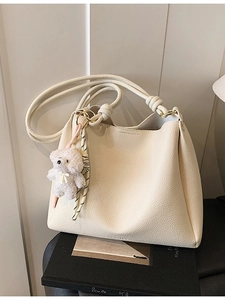 Sac seau minimaliste en cuir crème avec poignée nouée et breloque ours posé sur des livres