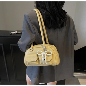 Detail of yellow pebbled leather shoulder bag featuring twin front flap pockets and pearl bow