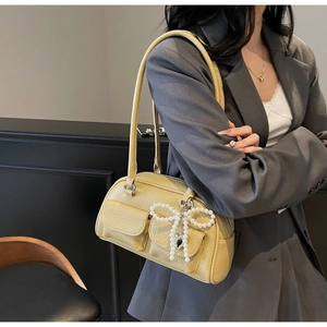 Detail of yellow lychee leather bag with front pockets and pearl bow charm accessory