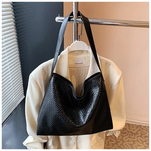 Close-up of a black textured leather hobo bag hanging on a white professional blazer