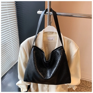 Detailed view of black woven tote bag with smooth glossy finish on a white suit