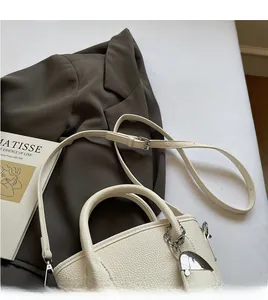 Detail of white lychee leather handbag with adjustable long strap and silver hardware charm