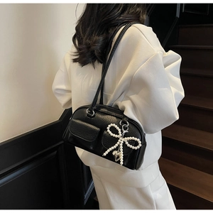 Detail of black lychee leather shoulder bag with white pearl bow pendant and mini pockets