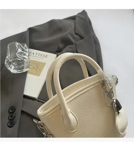 Close-up of white lychee leather bucket bag with silver hardware on grey blazer suit