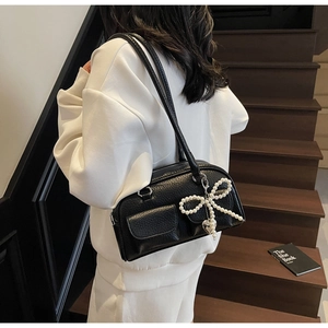 Detail of black leather pillow bag featuring pearl bow charm and dual front pockets