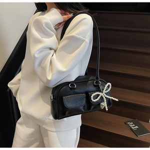 Close-up of black lychee leather bag with front pockets and pearl bow heart charm