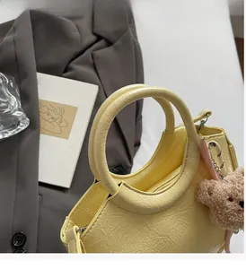 Close-up of yellow pleated bucket bag with round handle and plush bear charm detail