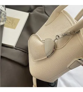 Detail of cream white lychee grain leather bucket bag with metallic heart charm accessory