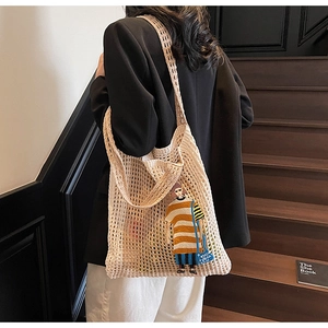 Detail der beigefarbenen Stricktasche mit modischem Aufnäher an einem Model