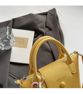 Détail d'un sac à main jaune en cuir grainé avec boucles argentées sur un blazer gris