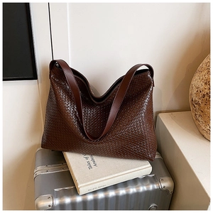 Detail of dark brown woven tote bag with diagonal weave texture on a silver suitcase