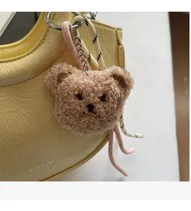 Close-up of a plush bear charm with woven strap on a textured cream leather bucket bag