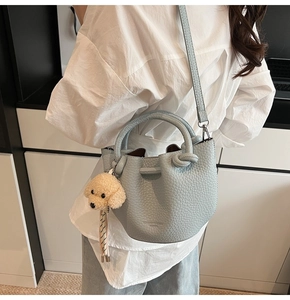 Détail du sac seau bleu clair avec texture cuir grainé et un joli pendentif ours