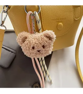 Détail d'un charme d'ours en peluche beige avec corde tissée et fermoir argenté sur un sac