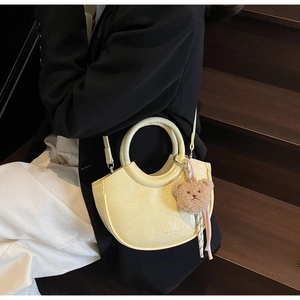 Close-up of yellow crescent bag with textured glossy leather and plush bear pendant