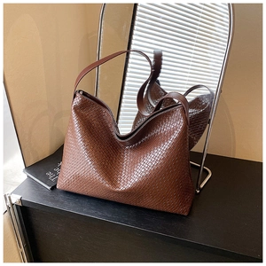 Detail of dark brown woven hobo bag with thick leather strap on a sleek black surface