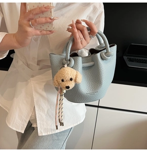 Detail of light blue pebble leather bucket bag with a plush dog charm and knotted handle
