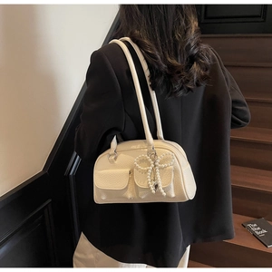 Detail of cream white leather pillow bag with pearl bow charm and twin straps on model