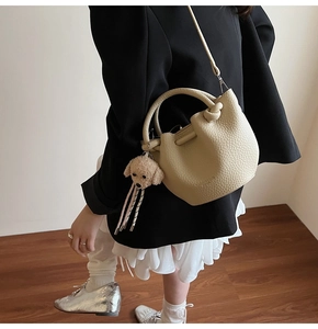 Detail of beige lychee pattern bucket bag with knot handle and poodle plush pendant