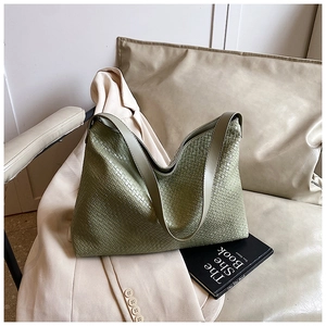 Detail of green woven leather shoulder bag showing intricate Intrecciato texture on a sofa