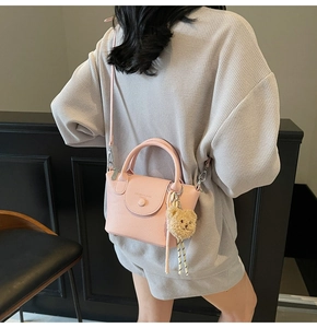 Detail of pink lychee leather bucket bag with plush bear charm and striped scarf on model