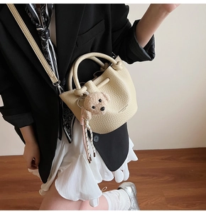 Détail du sac seau en cuir grainé crème avec breloque peluche et bandoulière