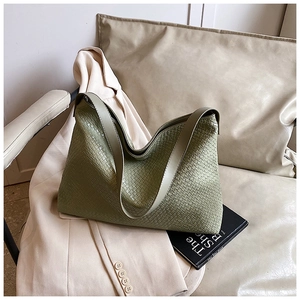 Detail of green woven tote bag with wide strap on beige blazer, close-up texture
