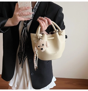 Detail of off-white lychee grain leather bucket bag with knotted handle and plush puppy charm