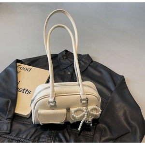 Detail of cream pebbled leather bowling bag with pearl bow charm on black leather jacket