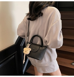 Chic black lychee leather bucket bag with cute bear charm shown on model in a grey outfit
