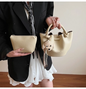 Detail of beige lychee pattern bucket bag with knot handle and plush dog charm accessory