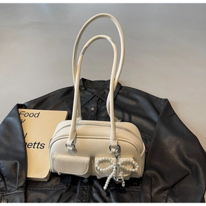Close-up of cream white leather bowling bag with twin flap pockets and pearl bow charm