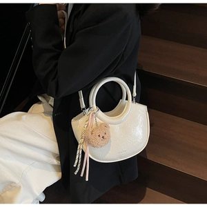 Detail of white pleated bucket bag with bear pendant and decorative cord shown on a model