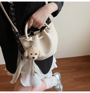 Detail of creamy white bucket bag featuring litchi texture and cute plush puppy charm