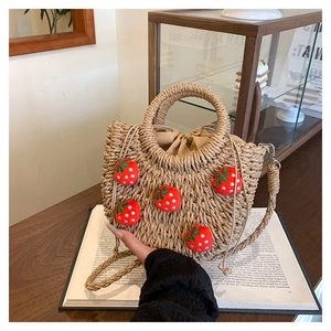 Detail der Strohhandtasche mit roten Plüsch-Erdbeeren auf einem Holztisch