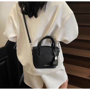 Detail of black lychee grain leather bucket bag with silver heart charm and crossbody strap