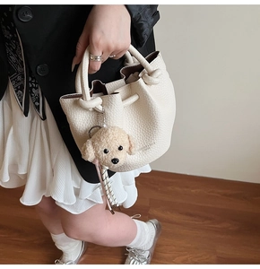 Detail of cream bucket bag with lychee texture, knot handles, and plush dog charm