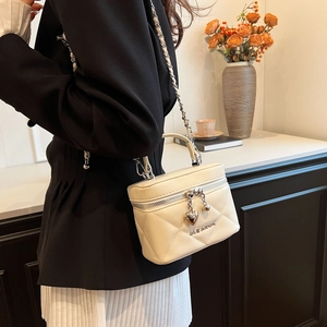 Close-up of cream quilted vanity bag with heart charms and silver chain strap